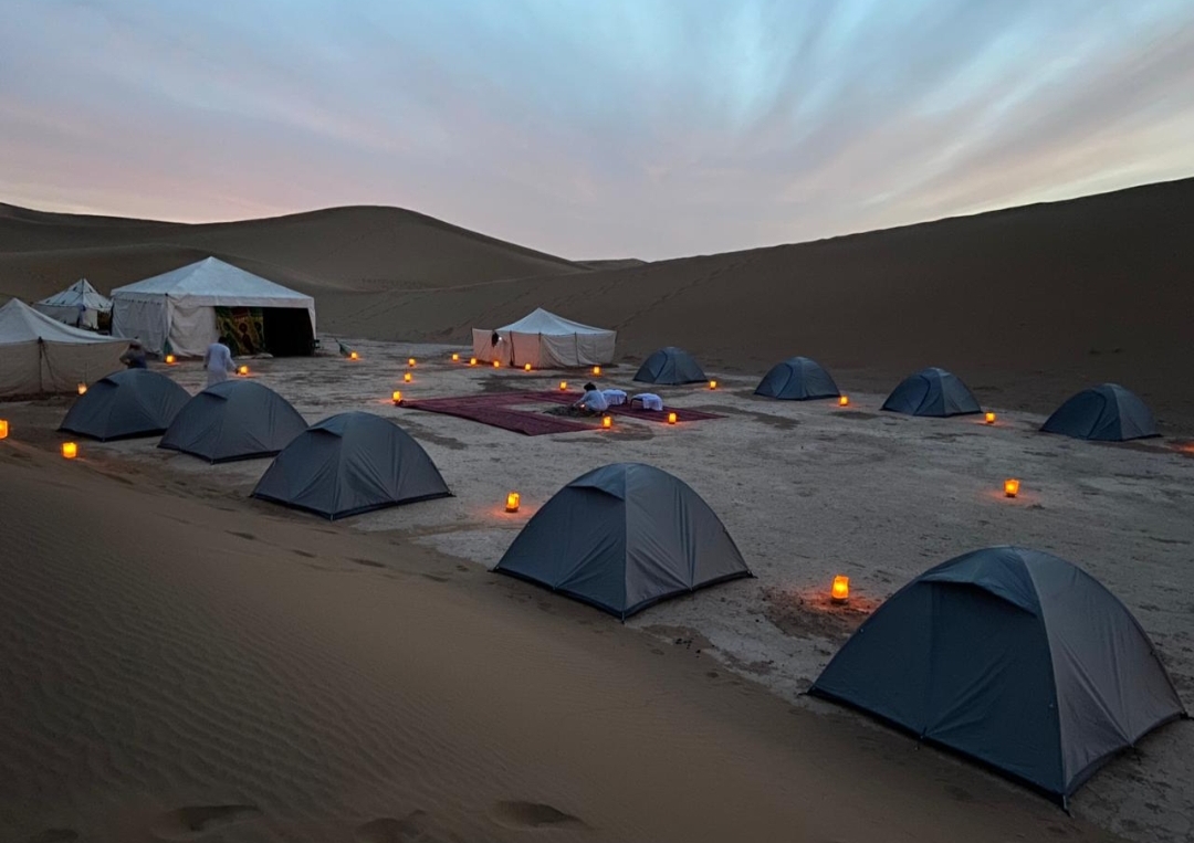 Campement de bivouac illuminé de lanternes dans les dunes de l'Erg Chegaga