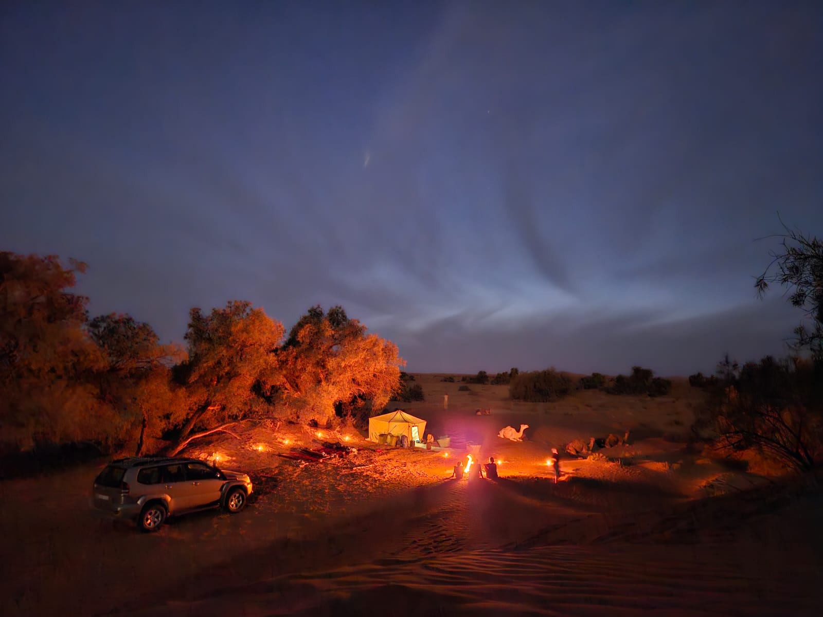 Bivouac au crépuscule avec véhicule 4x4 Prado, feu nomade et dromadaire